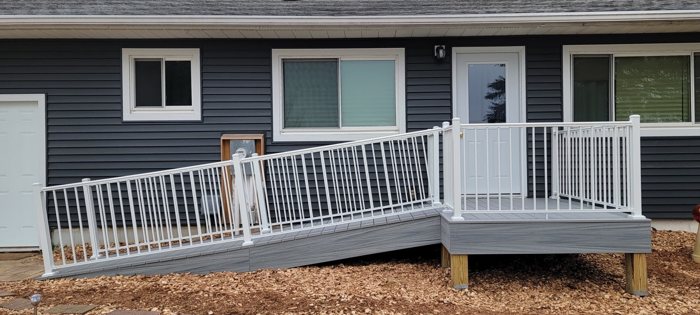 Composite deck with an accessible ramp and white railing leading to a home's back entrance