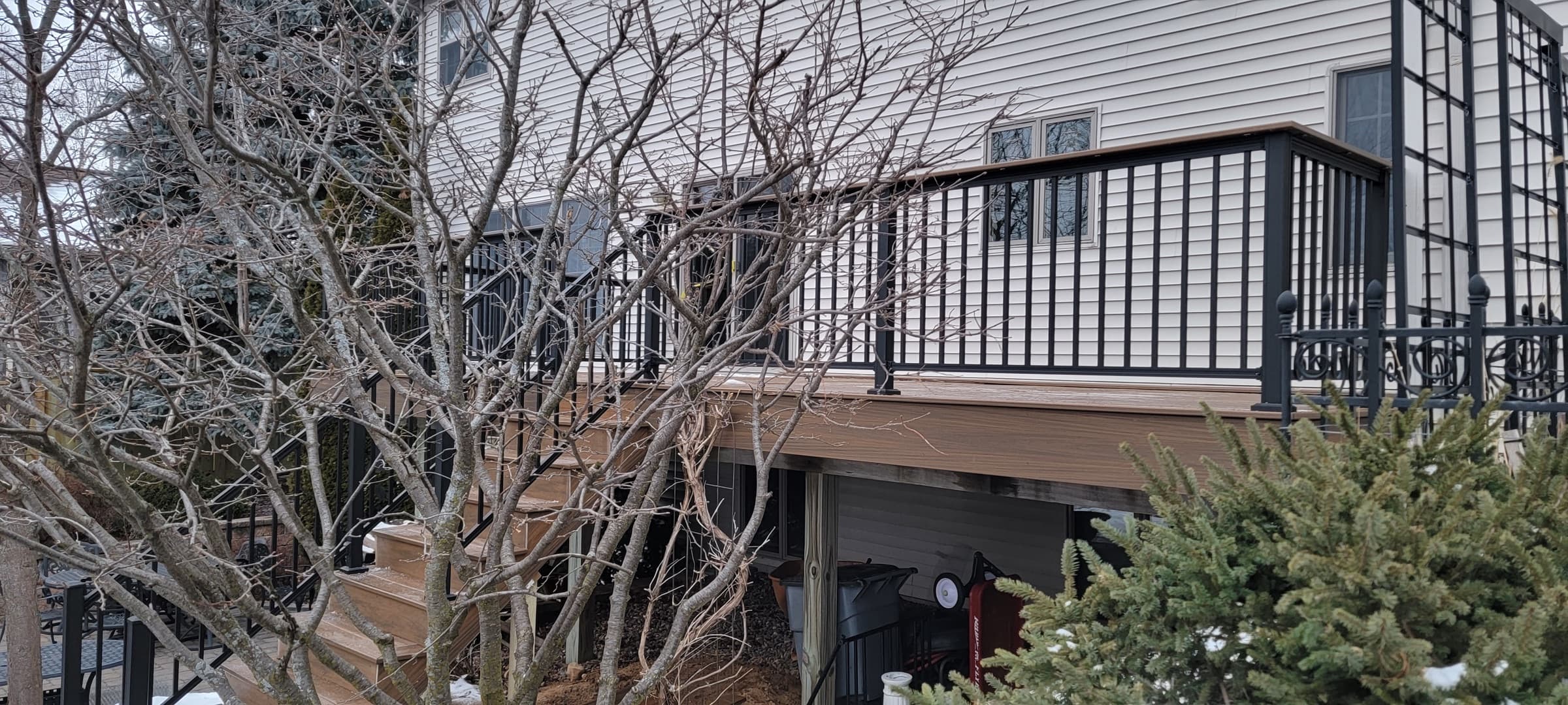 Elevated composite deck with black metal railing along the back of a home